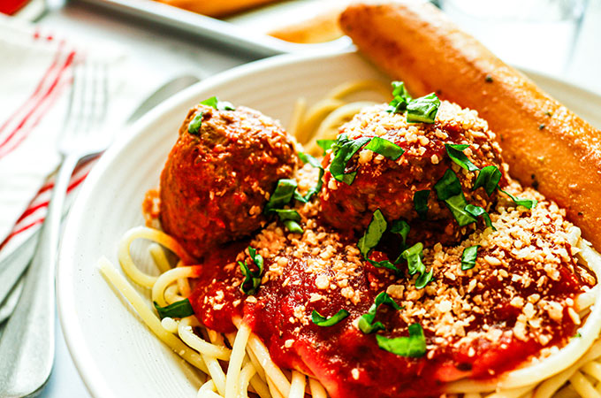 Bowl of spaghetti and meatballs in a marinara sauce with a garlic breadstick on the side